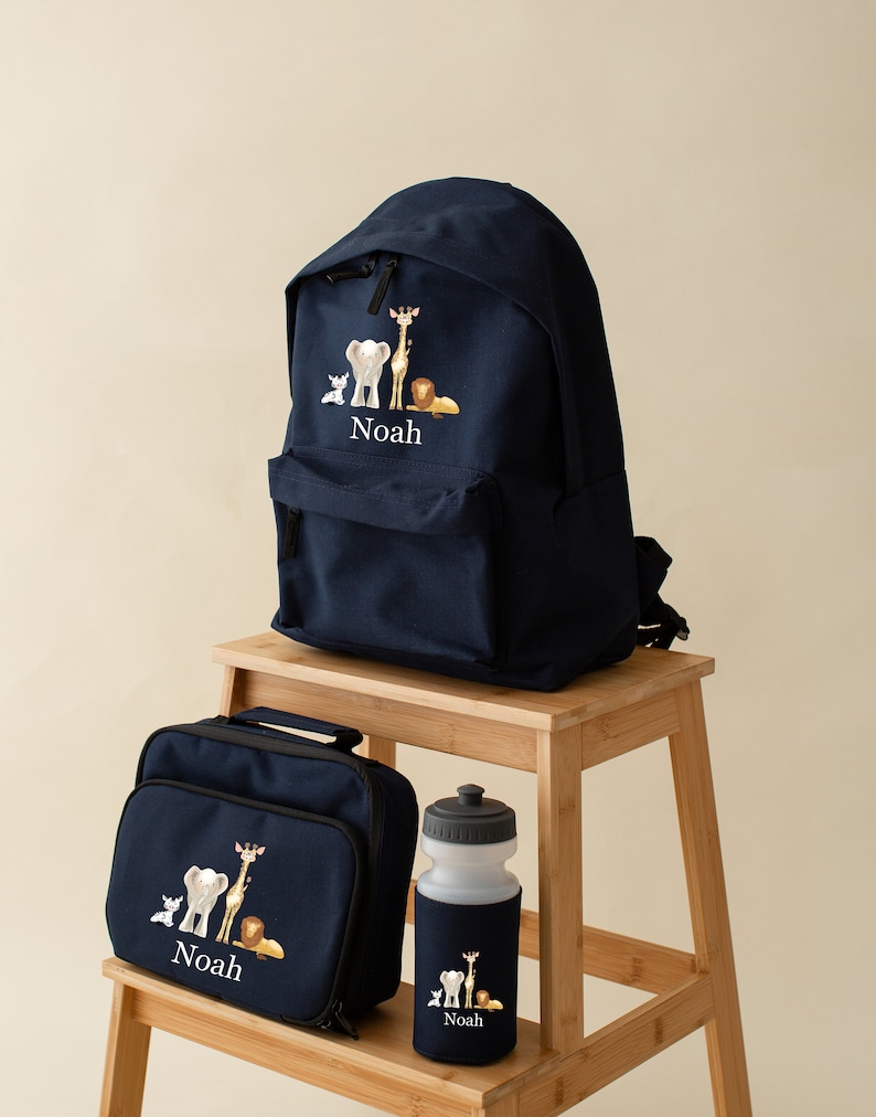 May include: A navy blue backpack, lunch bag, and water bottle set with a safari animal design and the name "Noah" embroidered on each piece.