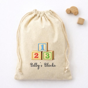 May include: A beige drawstring bag with the text "Billy's Blocks" and three wooden blocks numbered 1, 2, and 3. A small wooden car and a wooden cube are next to the bag. The blocks have blue, red, and green numbers.