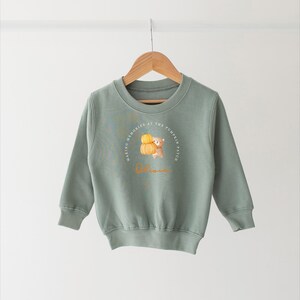 May include: A light green sweatshirt featuring a graphic of a bear holding a pumpkin. The graphic is encircled by text that reads "Making memories at the pumpkin patch" and the name "Olivia".
