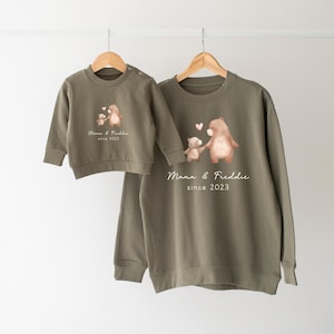 May include: Two green sweatshirts with a bear and cub design. The larger sweatshirt has the text "Mama & Freddie since 2023" printed on it. The smaller sweatshirt has the text "Mama & Freddie since 2023" printed on it.