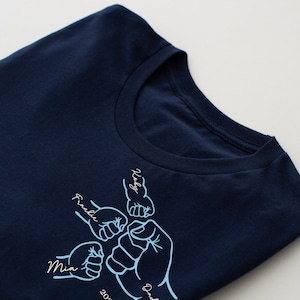 May include: A navy blue t-shirt with a design of five fists bumping each other. The fists are labeled with the names "Mia", "Frankie", "Daddy", "Koby", and the year "2024".