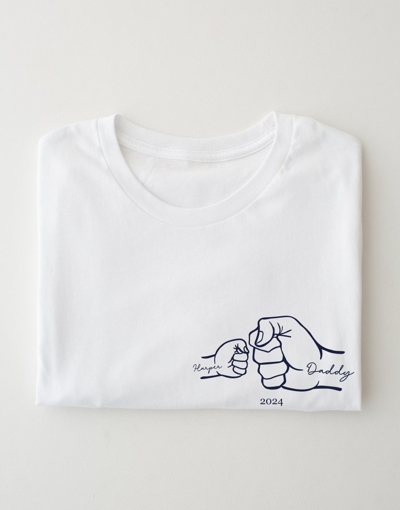 May include: White t-shirt with a blue graphic of two fists bumping, one labeled "Harper" and the other "Daddy" with the year 2024 below.