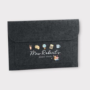 May include: A grey felt folder with a white label that says "Mrs. Robert's paper work" and has a row of colourful school-themed icons above the text.