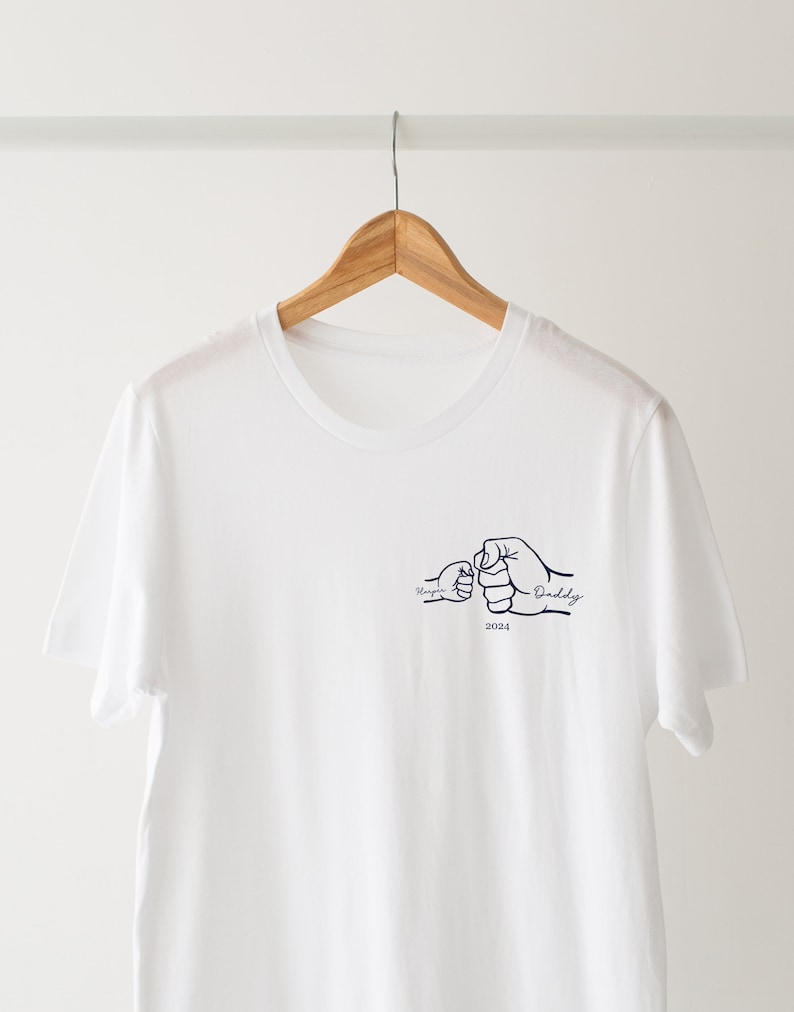 May include: White t-shirt with a navy blue design of two fists bumping, one labeled "Daddy" and the other "My Guy", with the year "2024" below.