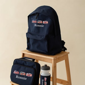May include: A navy blue backpack, lunch bag, and water bottle set. Each item features a colourful illustration of fire engines and the name "Ronnie" in white. The water bottle has a black lid and a navy blue sleeve.