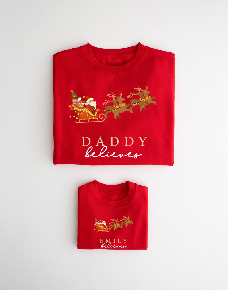 May include: Two red Christmas shirts with a Santa Claus and reindeer design. The larger shirt says "Daddy believes" and the smaller shirt says "Emily believes".