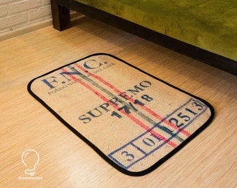 May include: A brown and black doormat with the text "F.N.C. FONDO NAZIONALE DEL CAFFE" and "SUPREMO 117/18" in white. The doormat has a black border and red, white, and blue stripes.