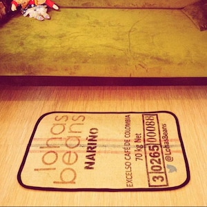 Könnte beinhalten: Eine braune und beige Fußmatte mit schwarzem Text, der "lonas beans Marino Excelso Café de Colombia 70 kg Net 3102651000883 @LobasBeans" lautet.