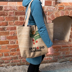 May include: A brown canvas tote bag with the text "Cafés do Brasil" and a green leaf design. The bag has a brown button closure.