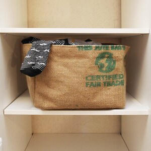 May include: A brown burlap storage bin with a green logo that says "This jute bag is made with certified fair trade" and a green recycling symbol. The bin is filled with black and white striped socks.