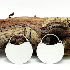May include: A pair of silver-toned hoop earrings featuring a flat, semi-circular disc design. The earrings have a smooth, matte metallic finish and a thin, curved wire closure that connects to the top of the circular metal plate structure.