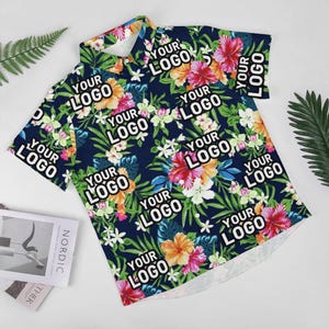 May include: A navy blue short-sleeved button-down shirt with a tropical floral print. The shirt features the text "YOUR LOGO" repeated throughout the design.
