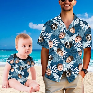 May include: A matching set of clothing featuring a blue floral pattern with faces of dogs and people. The set includes a short-sleeved button-down shirt and a baby bodysuit. The background is a beach scene with blue sky and sand.