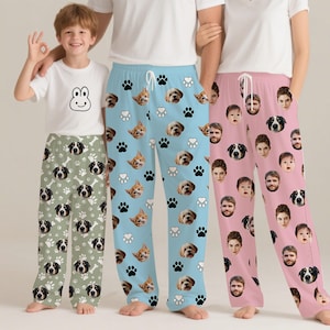 May include: Three pairs of pajama trousers are shown. One pair is sage green with dog faces, paw prints, and bones. Another is light blue with cat and dog faces and paw prints. The third is pink with faces.