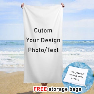 May include: White beach towel with the text "Cutom Your Design Photo/Text" printed on it. The towel is being held by a person on a beach.