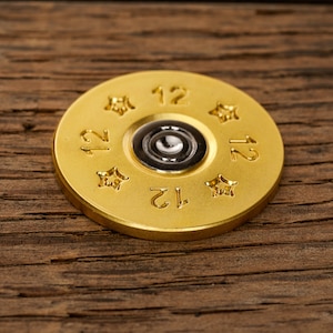 May include: A gold-colored shotgun shell with the number "12" printed on it four times. The shell has a star-shaped design around the rim.