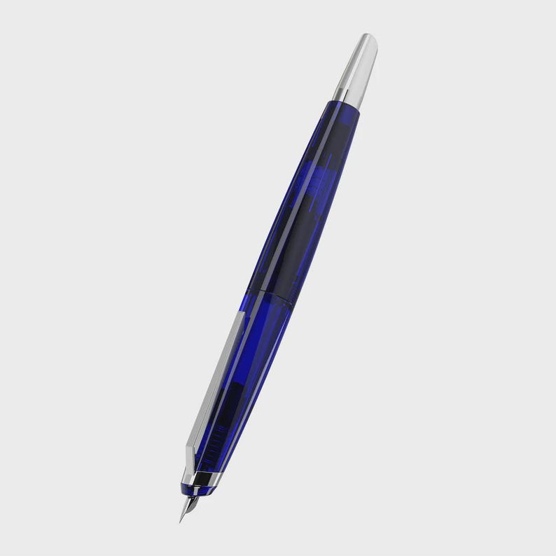 May include: A blue and silver fountain pen with a transparent barrel featuring a dark blue pattern. The pen has a silver nib and a silver cap. The pen is angled against a white background.