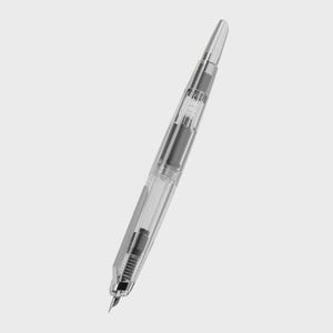May include: A clear fountain pen with a silver-colored tip and accents. The pen's body is transparent, revealing the internal ink mechanism. The pen is angled diagonally against a plain background.