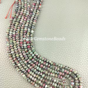 Puede incluir: Hebras de cuentas de piedras preciosas multicolores, con tonos rosas, verdes y grises. Las pequeñas cuentas facetadas están ensartadas en hilo rojo. El texto "JaipurGemstoneBeads" es visible.