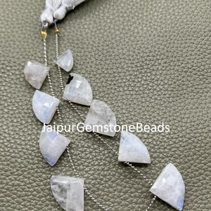 Op de afbeelding: Een streng maansteen edelsteen kralen met een witte kwast. De kralen zijn halfrond, met een mix van witte en blauwe tinten. De tekst "JaipurGemstoneBeads" is zichtbaar.
