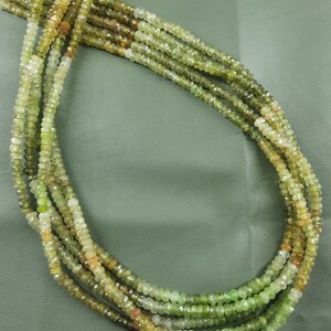 May include: A strand of green and yellow gemstone beads. The beads are faceted and have a slightly irregular shape. The beads are strung on a clear thread.