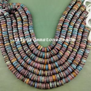 May include: A strand of multi-colored round beads, each bead is a different shade of blue, purple, pink, and brown. The beads are all about 1/2 inch in diameter and have a rough, textured surface. JaipurGemstoneBeads is printed on the image.