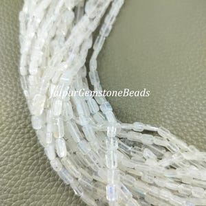 May include: A strand of white moonstone beads, each bead is rectangular and has a slight iridescent shimmer. The beads are strung together on a clear thread.