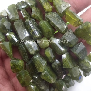 以下が含まれることがあります： ダークグリーンのファセットカットされたジェムストーンビーズのストランド。ビーズは不規則な形をしていて、ざらざらとした自然な質感があります。ビーズは透明な糸に通されており、ジュエリー作りに最適です。