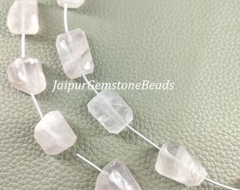 May include: A strand of light pink rose quartz beads, each bead is faceted and has a unique shape. The beads are strung on a silver wire and are displayed on a light green surface. JaipurGemstoneBeads is printed on the surface.