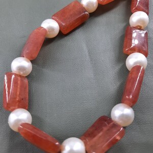 Puede incluir: Un collar hecho de cuentas rectangulares rojas y cuentas redondas blancas alternadas.