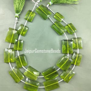 May include: A strand of green gemstone beads, each bead is a rectangular shape with a faceted cut. The beads are strung on a silver wire and have a tassel at each end.