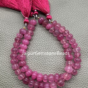May include: Strands of pink gemstone beads with a carved pumpkin shape. The beads are strung together and are accompanied by a pink tassel. The text "JaipurGemstoneBeads" is visible on the image.