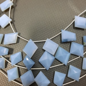 May include: A strand of light blue gemstone beads strung on a silver wire. The beads are square shaped with a slightly pointed top.