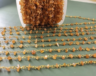 May include: A gold chain with small, irregular, orange-brown gemstone beads. The chain is laid out in rows on a green surface.