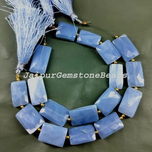 Puede incluir: Una hebra de cuentas de piedras preciosas azul claro con separadores dorados. Las cuentas son rectangulares y tienen un acabado liso y pulido. La hebra mide aproximadamente 45 cm de largo.