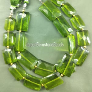 May include: A strand of green gemstone beads with gold spacers. The beads are faceted and have a rectangular shape. The beads are strung on a clear elastic cord. JaipurGemstoneBeads is printed on the image.