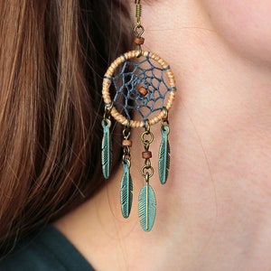 May include: A pair of dangle earrings featuring a dreamcatcher design with blue and brown string, and green feathers.