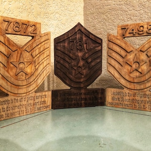 Peut inclure: Trois plaques en bois avec un insigne de grade militaire et une citation de Dwight D. Eisenhower. Les plaques sont teintées dans différentes nuances de brun. La citation dit : « Le leadership est l'art de faire faire à quelqu'un ce que vous voulez qu'il fasse parce qu'il veut le faire. » - Eisenhower
