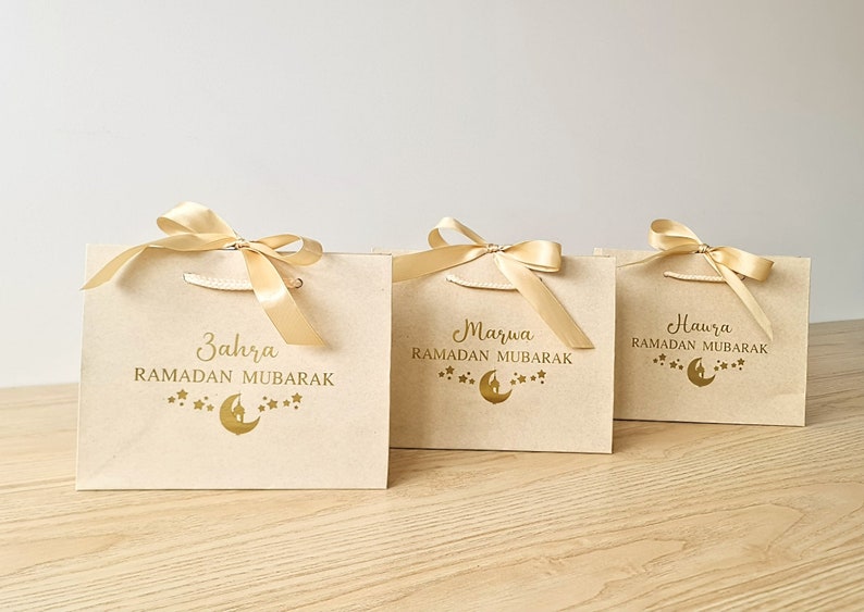 Personalised Eid Gift Bag - Moon & Stars Ramadan Mubarak
May include: Three cream gift bags with gold ribbon bows and gold lettering. The bags are decorated with a crescent moon and stars. The text on the bags reads "Zahra Ramadan Mubarak", "Marwa Ramadan Mubarak", and "Hawra Ramadan Mubarak".