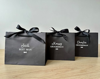May include: Three black gift bags with black satin ribbon bows. The bags are labeled with the names "Jack Best Man", "Harry Groomsman", and "Charlie Groomsman".