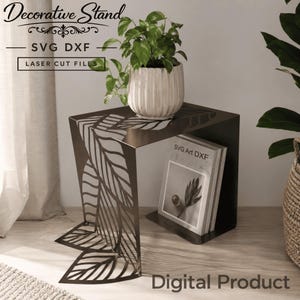 Może przedstawiać: Dekoracyjny metalowy stojak z motywem liści, trzymający roślinę doniczkową i książkę. Stojak zawiera tekst "SVG DXF LASER CUT FILES" i "Digital Product". Stojak jest w ciemnym metalicznym kolorze.
