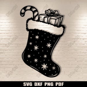 Puede incluir: Una silueta en blanco y negro de una media de Navidad con un bastón de caramelo y regalos dentro. La media está decorada con estrellas blancas.