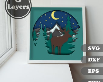 Puede incluir: Un diseño de papel recortado en capas que presenta un ciervo de pie en un bosque con montañas en el fondo. El diseño se coloca sobre un cielo nocturno azul con una luna creciente y estrellas. El diseño está enmarcado en blanco y tiene las palabras "SVG, DXF, EPS, PDF" impresas en el lado derecho.