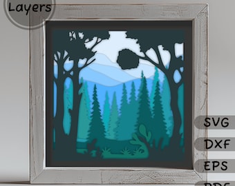 May include: A layered papercraft design of a forest scene with trees, mountains, and a blue sky. The design is in a wooden frame and has 13 layers. The design is available in SVG, DXF, EPS, and PDF formats.