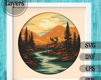 Puede incluir: Un diseño de papel en capas que presenta un ciervo de pie en un río con montañas y árboles en el fondo. El diseño está en un círculo y tiene un cielo de puesta de sol.