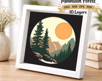 Peut inclure: Une œuvre d'art encadrée représentant une forêt de montagne en couches. L'œuvre présente un design circulaire avec une scène de forêt, comprenant des arbres, des montagnes et un soleil couchant. Le cadre est blanc, avec le texte "Layered Mountain Forest".