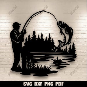 May include: Black silhouette of a fisherman catching a fish. The image features a lake, trees, and reeds. The text "SVG DXF PNG PDF" is at the bottom.