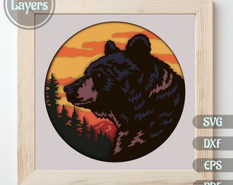 Puede incluir: Una silueta de oso negro con un fondo de puesta de sol en un círculo. El oso mira hacia la izquierda. La imagen es un diseño de artesanía en papel en capas con 9 capas.