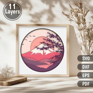 May include: A digital papercraft design featuring a layered, pink and purple mountain scene with a cherry blossom tree and a sun in the background. The design is in a circle and has 11 layers.