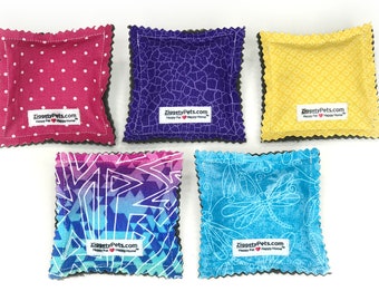 May include: Five colorful pet toys with patterned fabric. The toys feature various designs, including polka dots, geometric shapes, and floral patterns. Each toy has a black scalloped edge and a white label with the text "ZiggetyPets.com Happy Pet Happy Home".